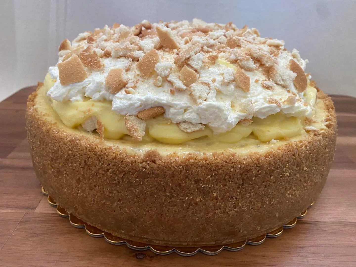 A banana cheesecake topped with whipped cream, banana slices and crushed vanilla wafers.