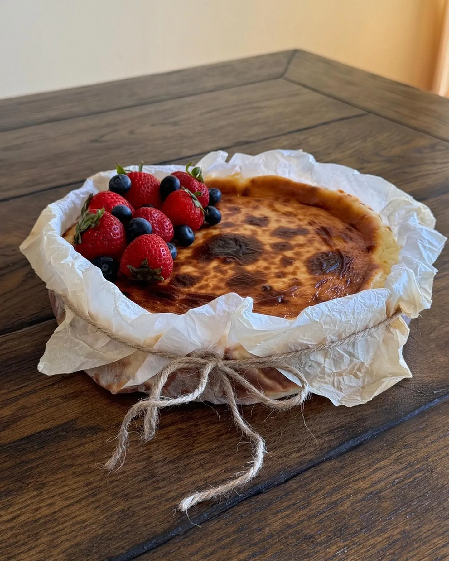 A burnished Basque cheesecake in parchment, topped with fresh strawberries and blueberries.