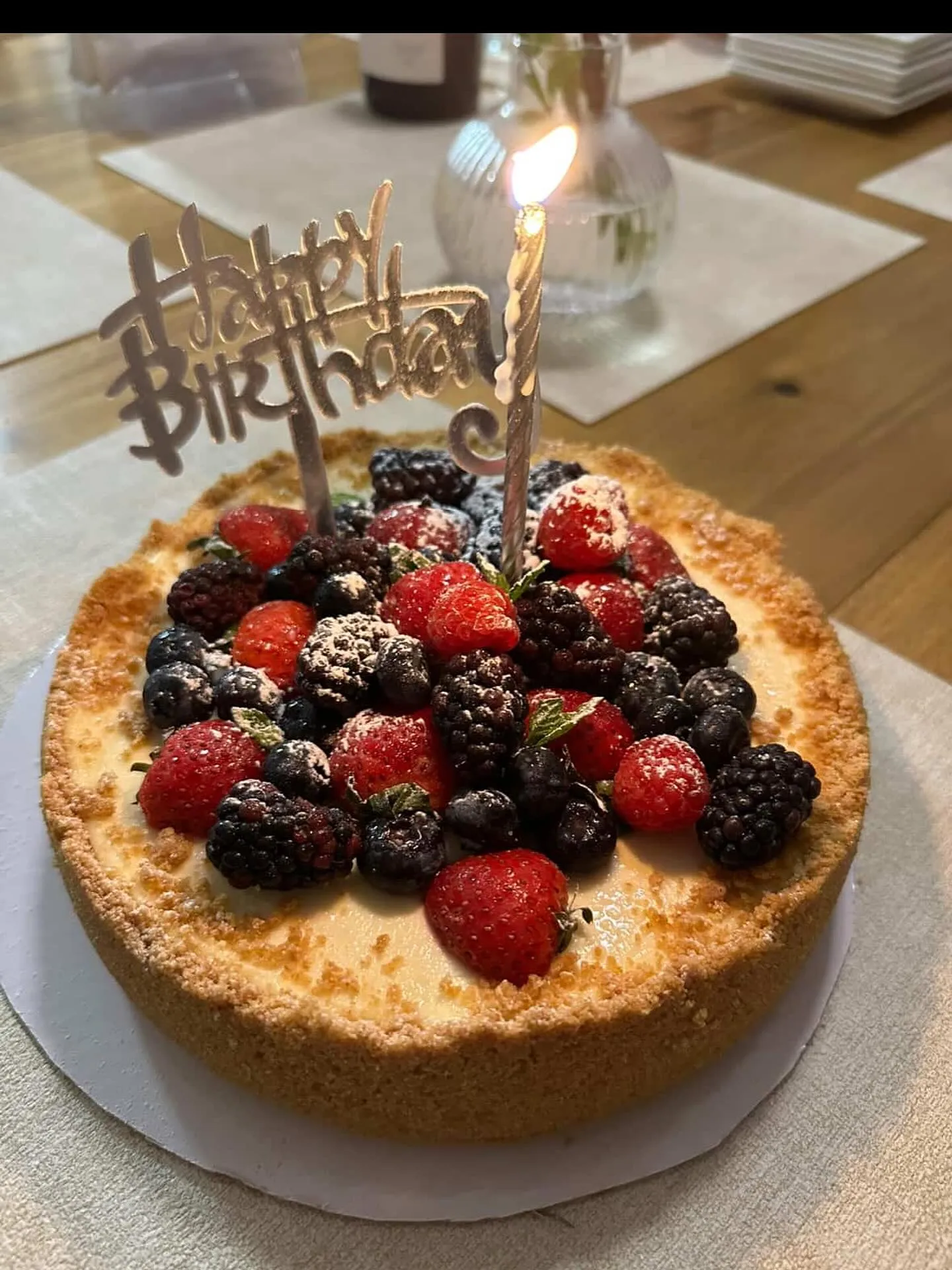A mixed-berry cheesecake with a Happy Birthday topper and a lit candle.