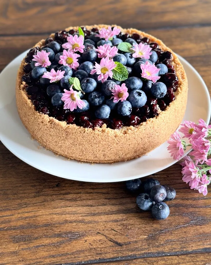 A creamy blueberry cheesecake topped with fresh blueberries and pink flowers.