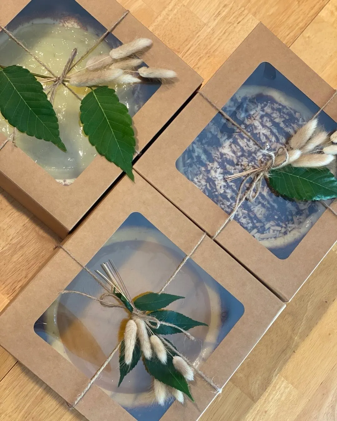 An assortment of boxed cheesecakes in kraft window boxes, decorated with greenery.