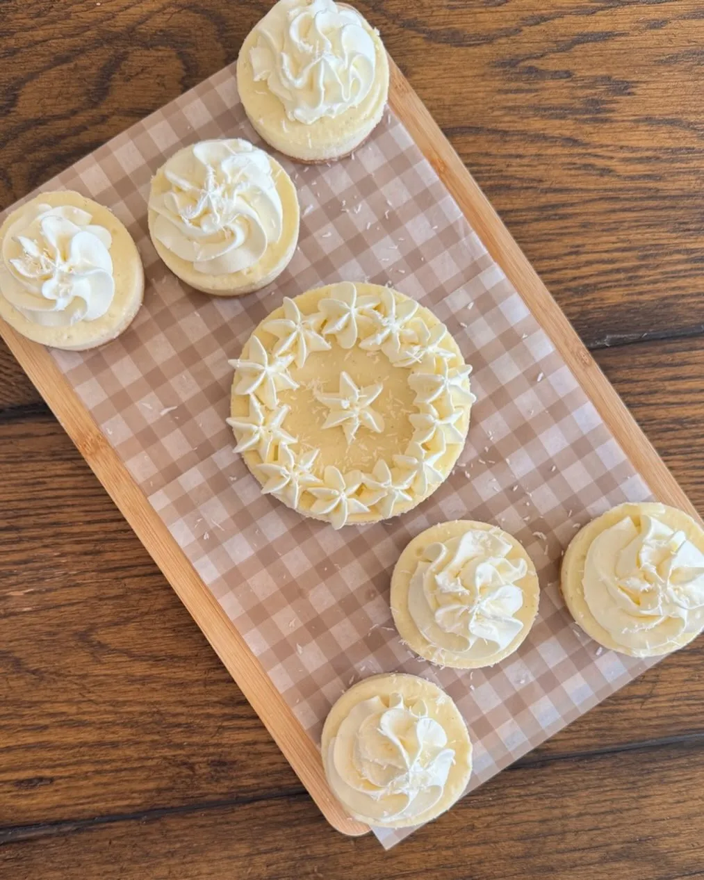 A small coconut cheesecake surrounded by mini coconut cheesecakes, each topped with whipped cream and coconut.