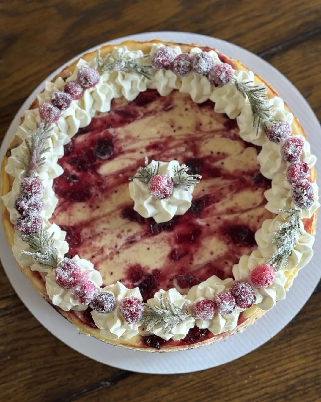 A cranberry-swirl cheesecake topped with sugared cranberries and frosted rosemary sprigs.