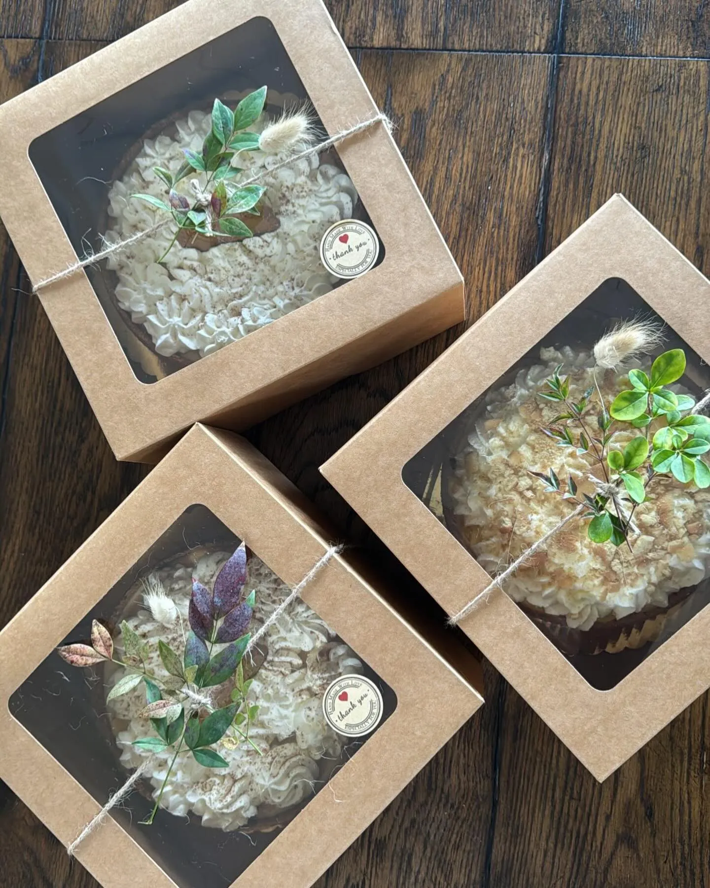 Cheesecakes packaged in kraft gift boxes, decorated with sprigs of greenery.