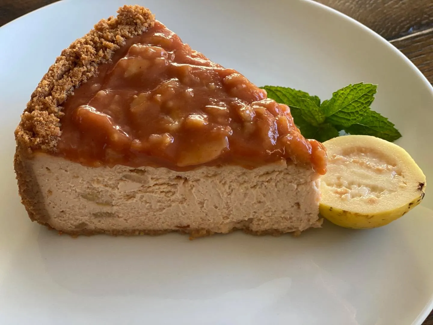 A slice of guava cheesecake topped with guava compote, served with fresh guava and mint.