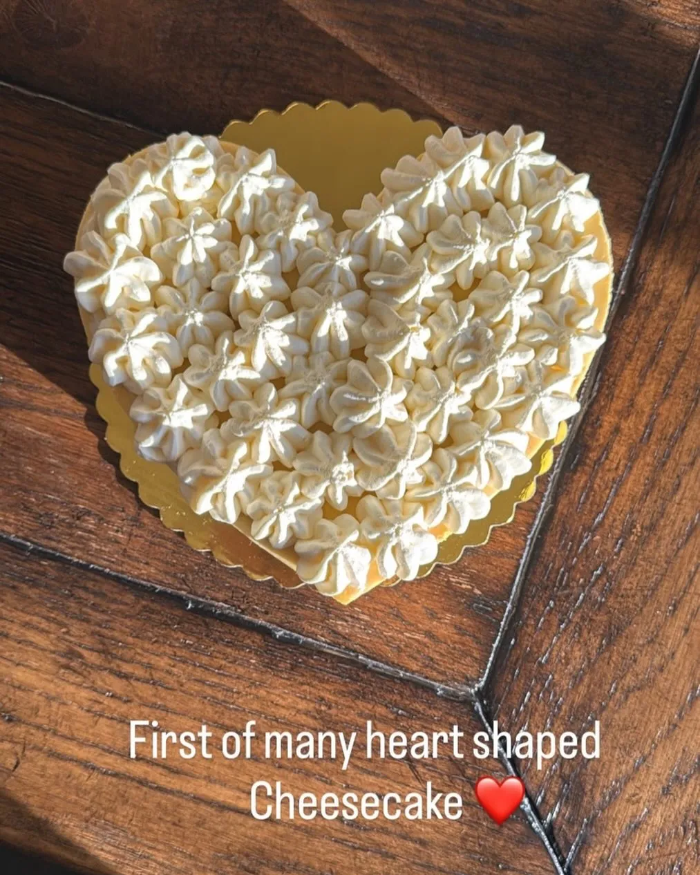 A heart-shaped cheesecake covered in whipped-cream florets on a gold board.