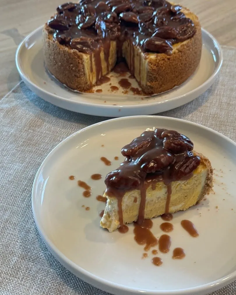 A pumpkin cheesecake topped with caramelised pecans and caramel, with a slice on a plate.