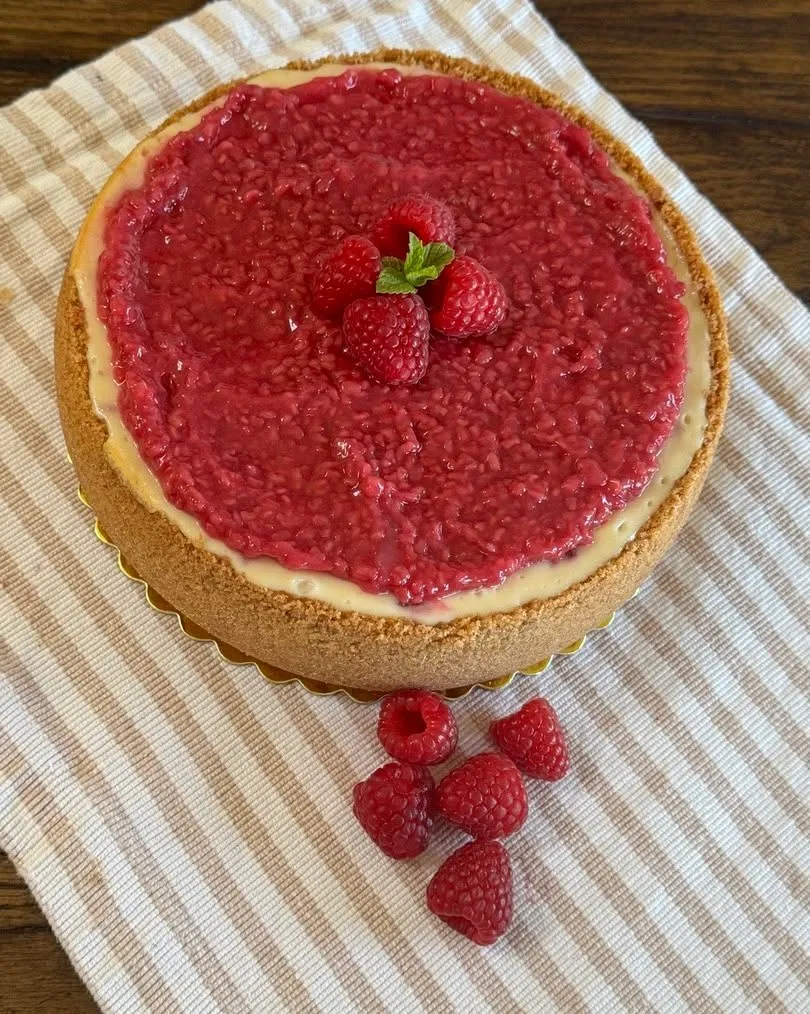 A raspberry cheesecake topped with raspberry sauce and fresh raspberries.