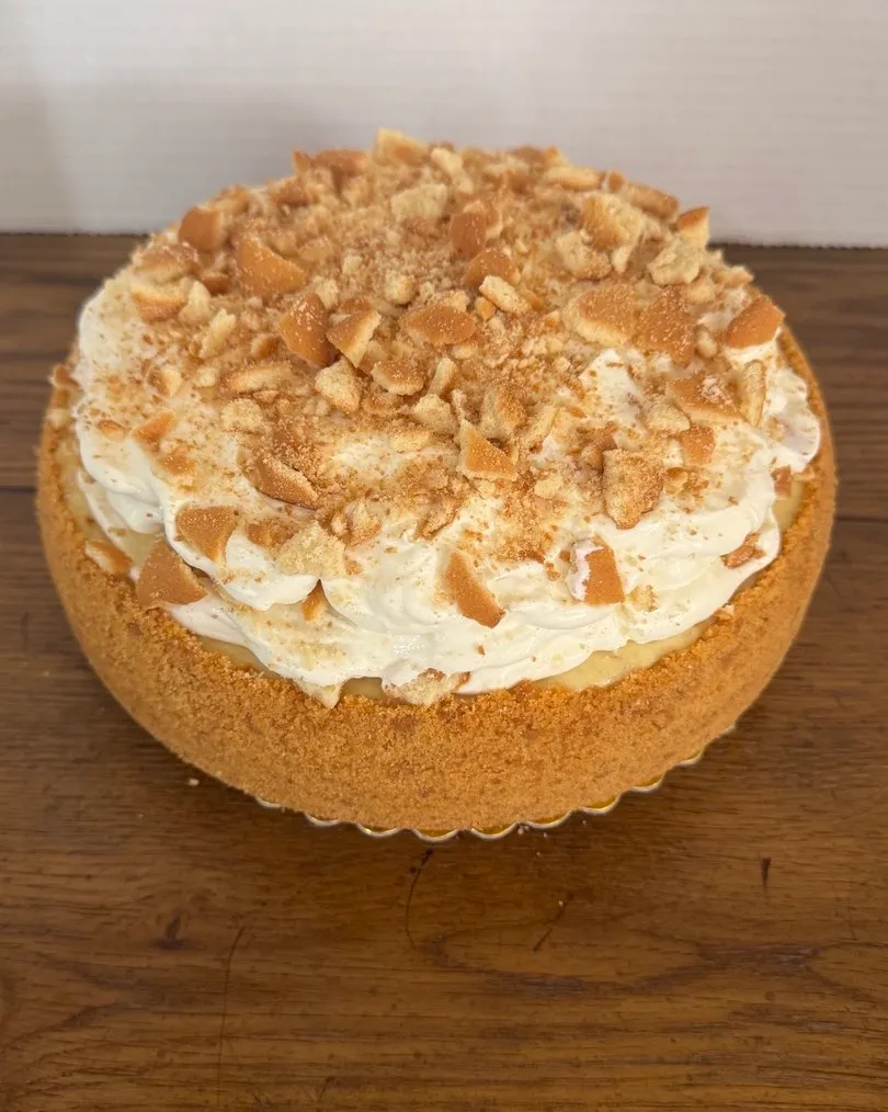 A cheesecake topped with whipped cream and crushed vanilla wafers.